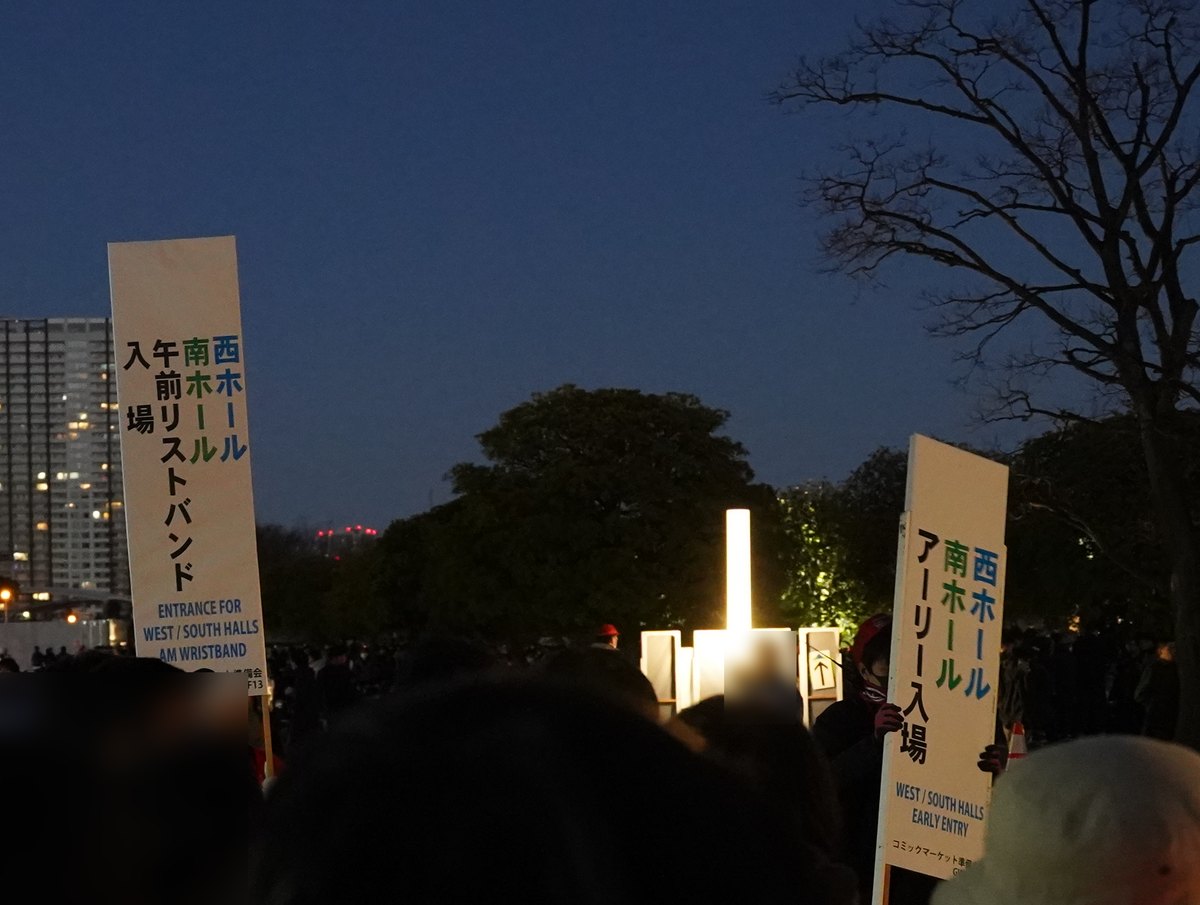 天還沒亮的會場外排隊人群中舉著兩塊直式看板:左邊寫「西ホール 南ホール 午前リストバンド入場」與英文 AM WRISTBAND,右邊寫「西ホール 南ホール アーリー入場」與英文 EARLY ENTRY,背景是深藍色天空與亮燈的高樓