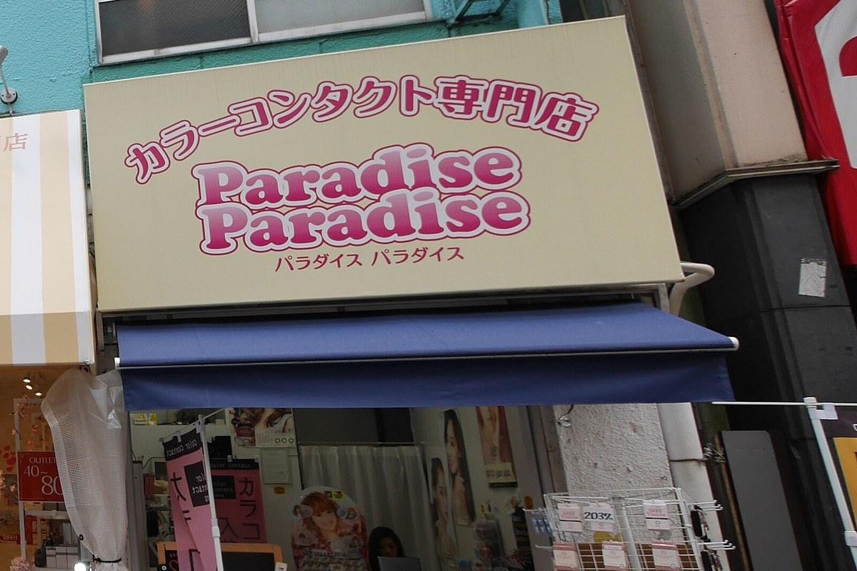 A colour contact lens specialty shop on a street in Shimokitazawa, Tokyo, its sign reading karaa kontakuto senmonten above product racks under the awning