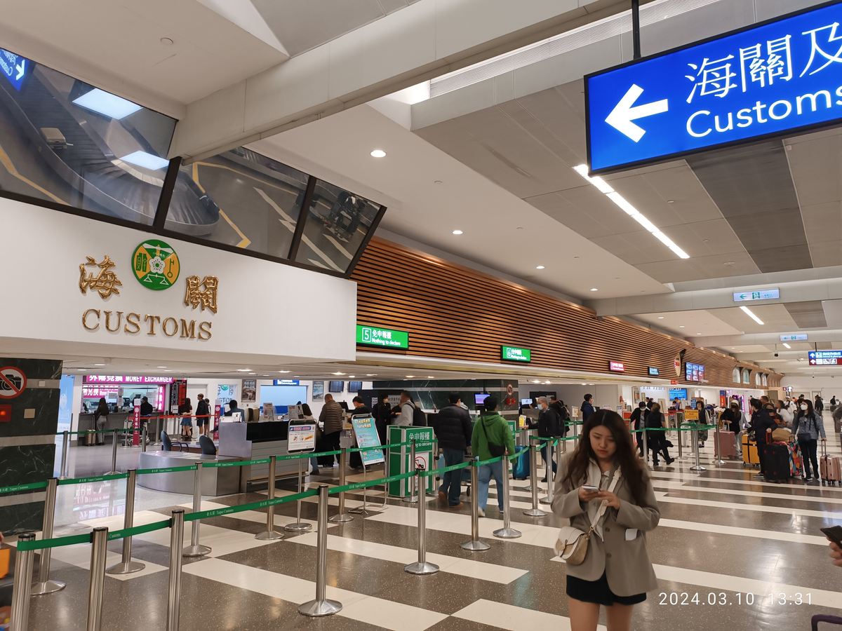 Customs area at Taoyuan International Airport arrivals, with the gold CUSTOMS emblem and a green Nothing to Declare desk sign above green Taipei Customs barrier tape