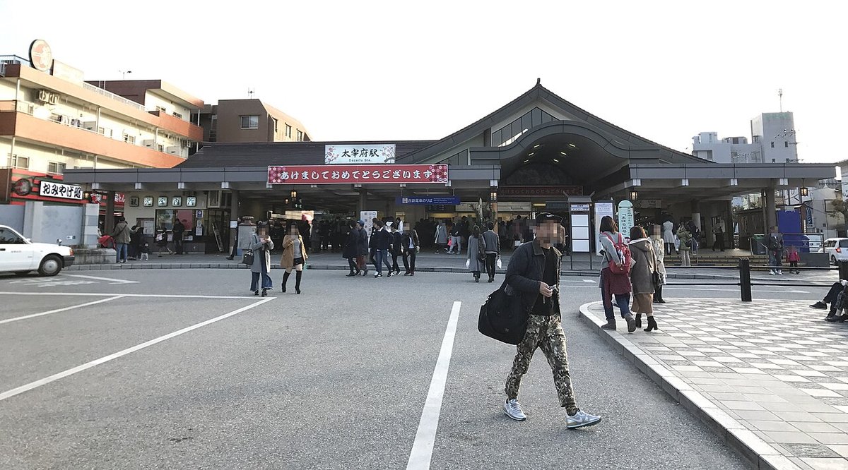 2017 年 1 月的西鐵太宰府站站前：灰瓦大屋頂的站舍，屋簷下掛著「太宰府駅」站名牌與紅底白字「あけましておめでとうございます」橫幅，站前廣場上有進出站的行人，左邊是掛著「おみやげ処」招牌的店