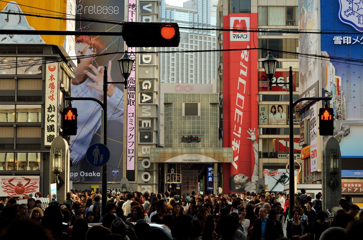 Neon billboards along the Dotonbori canal in Osaka with crowds on Ebisubashi bridge at night