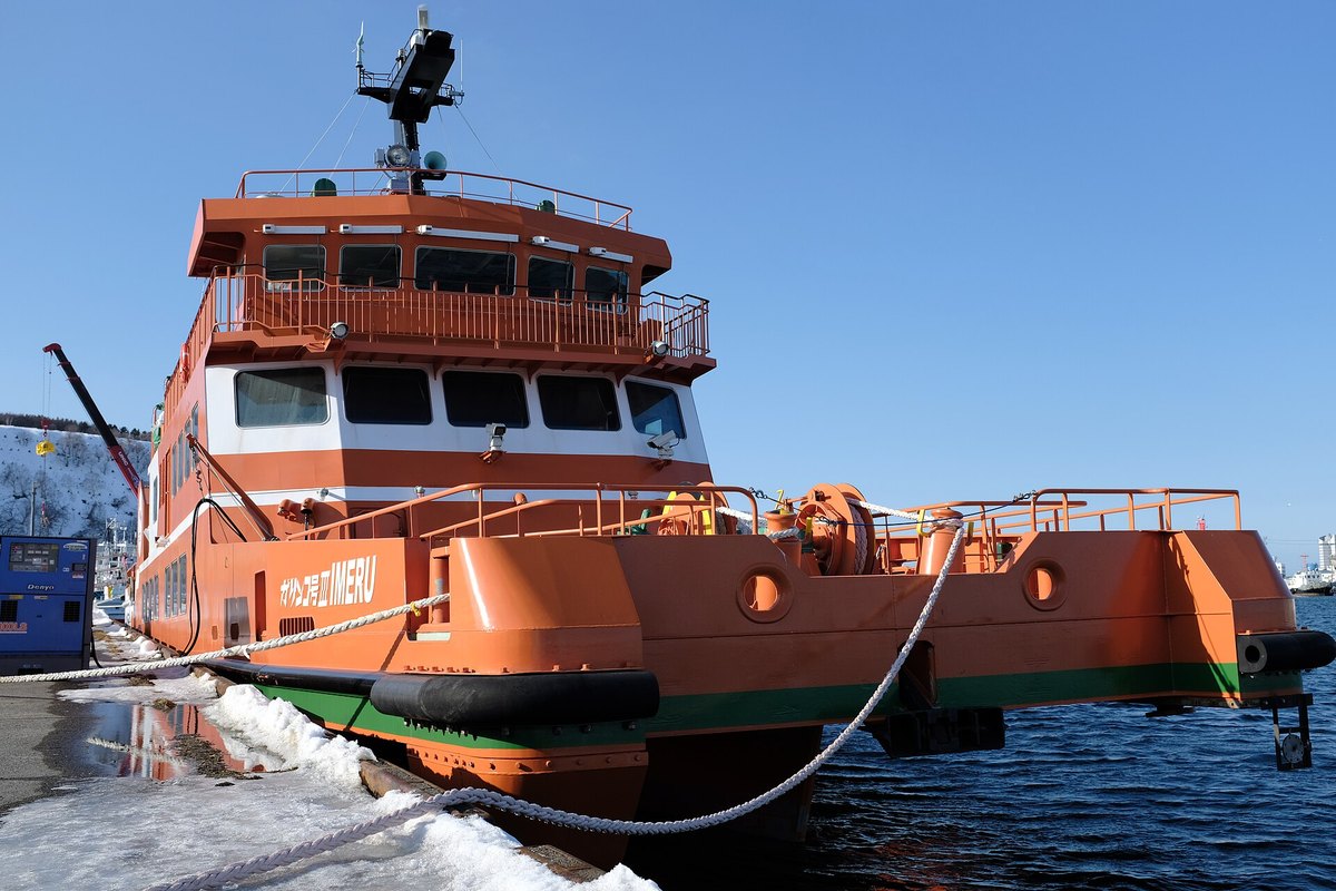 Garinko-go III IMERU alongside a quay: orange hull, white cabin, two railed decks, the ship's name in white on the side, and ice-free water