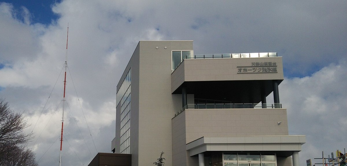 The Okhotsk Ryu-hyo Museum on Mt. Tento: a beige, box-shaped multi-storey building with its name in Japanese lettering on the wall, a glass-railed top level, and a red-and-white antenna mast to the left