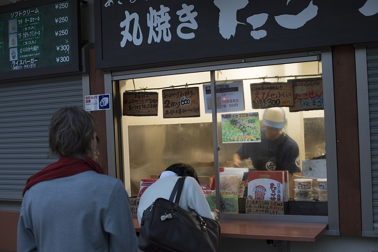 あさひ本店的窗口，職人正在鐵板前現壓丸焼きたこせんべい，遊客在窗外圍觀