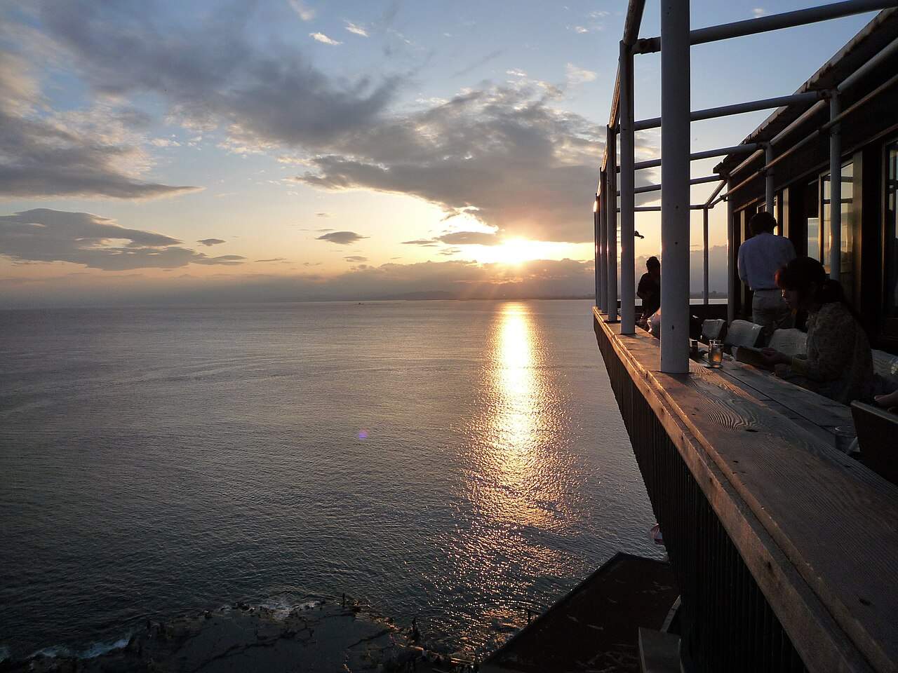 魚見亭的露天座位懸在崖邊，客人正對相模灣海面上的夕陽用餐