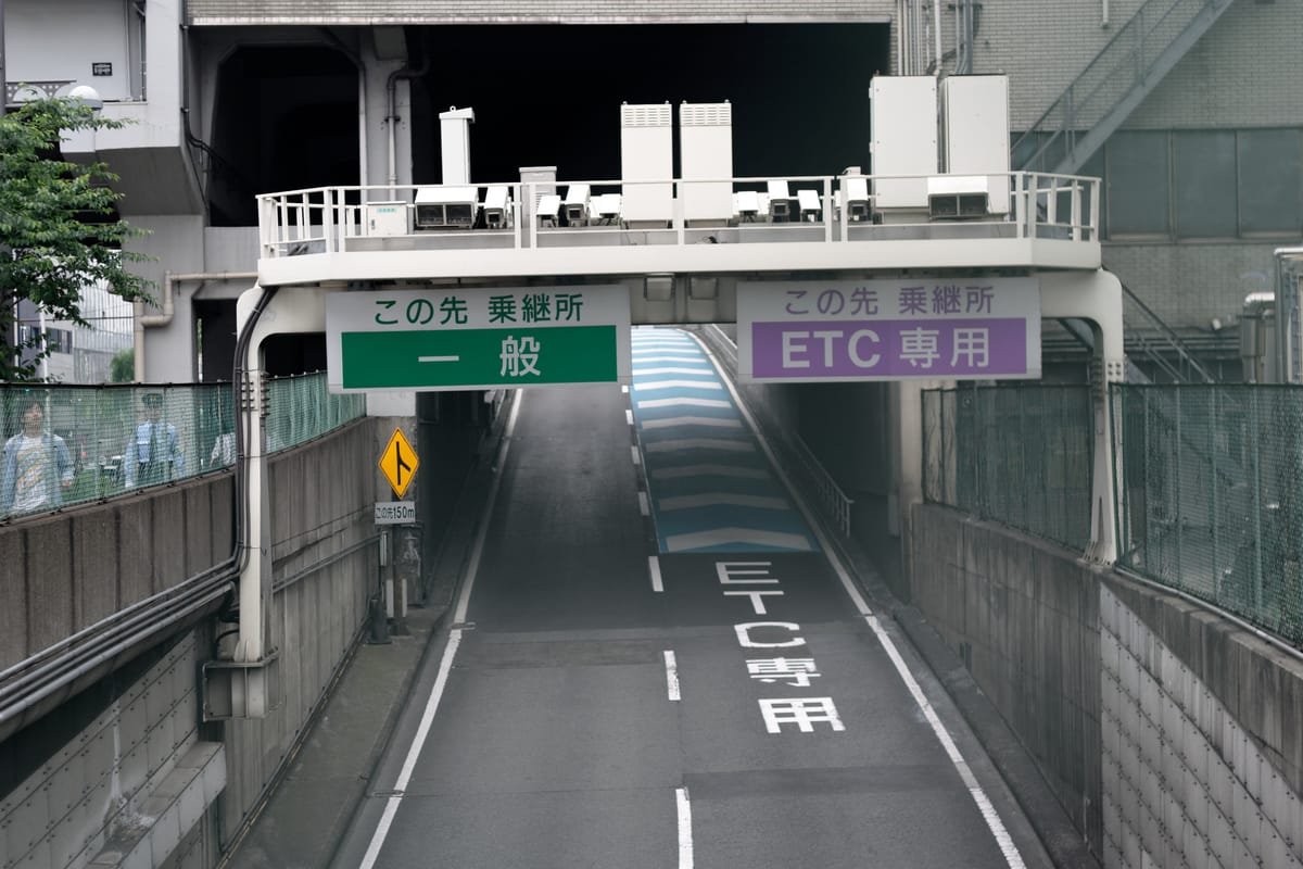 Lane-split signage on a Japanese urban expressway: a green sign reading ippan (general) on the left and a purple sign reading ETC senyo (ETC only) on the right, with ETC senyo also painted on the road surface