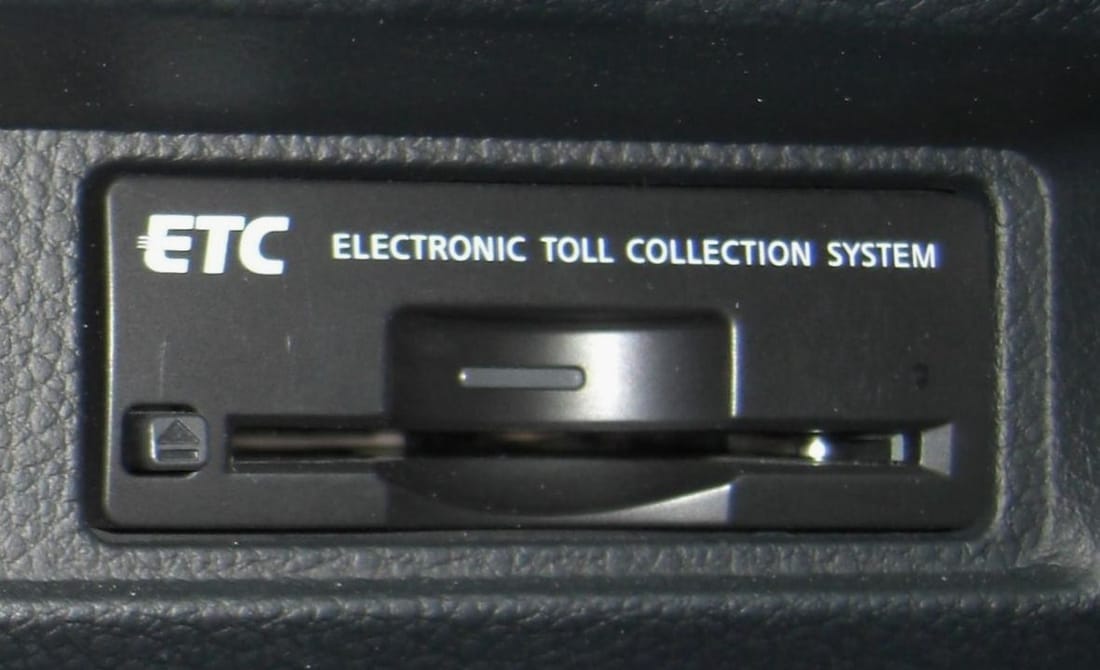 Close-up of a Japanese in-car ETC transponder marked ETC / ELECTRONIC TOLL COLLECTION SYSTEM, with the card slot across the centre and the eject button at left