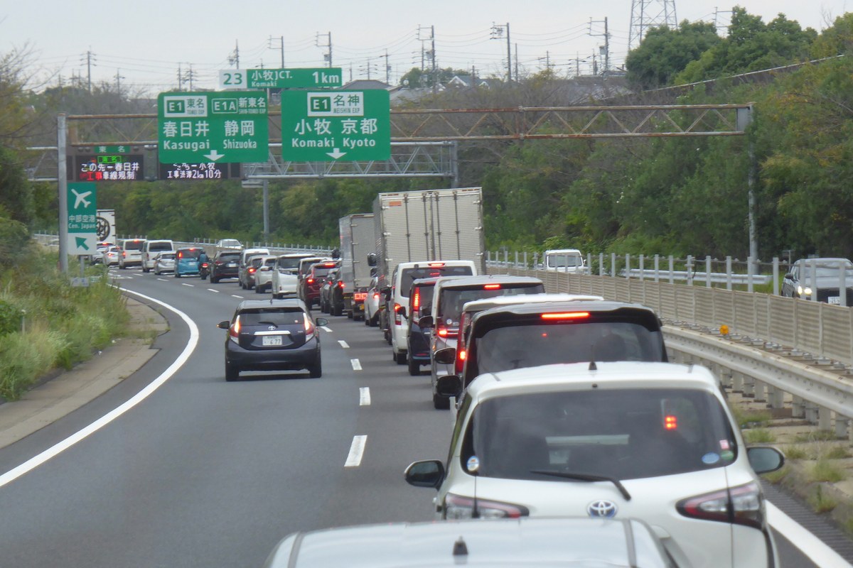Queued traffic on a Japanese expressway, cars backed up beneath the green overhead direction signs on the approach to Komaki junction
