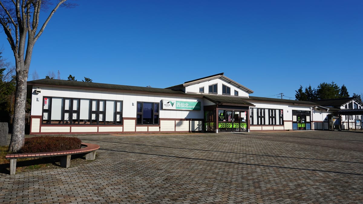 The building and paved forecourt of Nishisenboku Service Area on the Akita Expressway, with NEXCO East's green service-area sign above the entrance