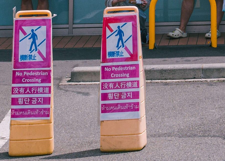 LAWSON 停車場邊兩個桃紅色立牌,畫著被斜線劃掉的行人,用日文、英文、中文、韓文、泰文寫著「横断禁止」「No Pedestrian Crossing」「没有人行横道」