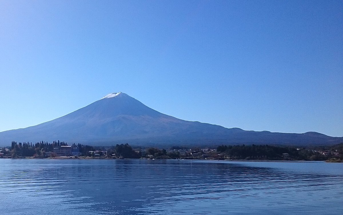 晴天從河口湖的湖面上看富士山:整座山是深藍色,只有山頂最上面一小塊是白的,山腳是湖岸的樹林與房子