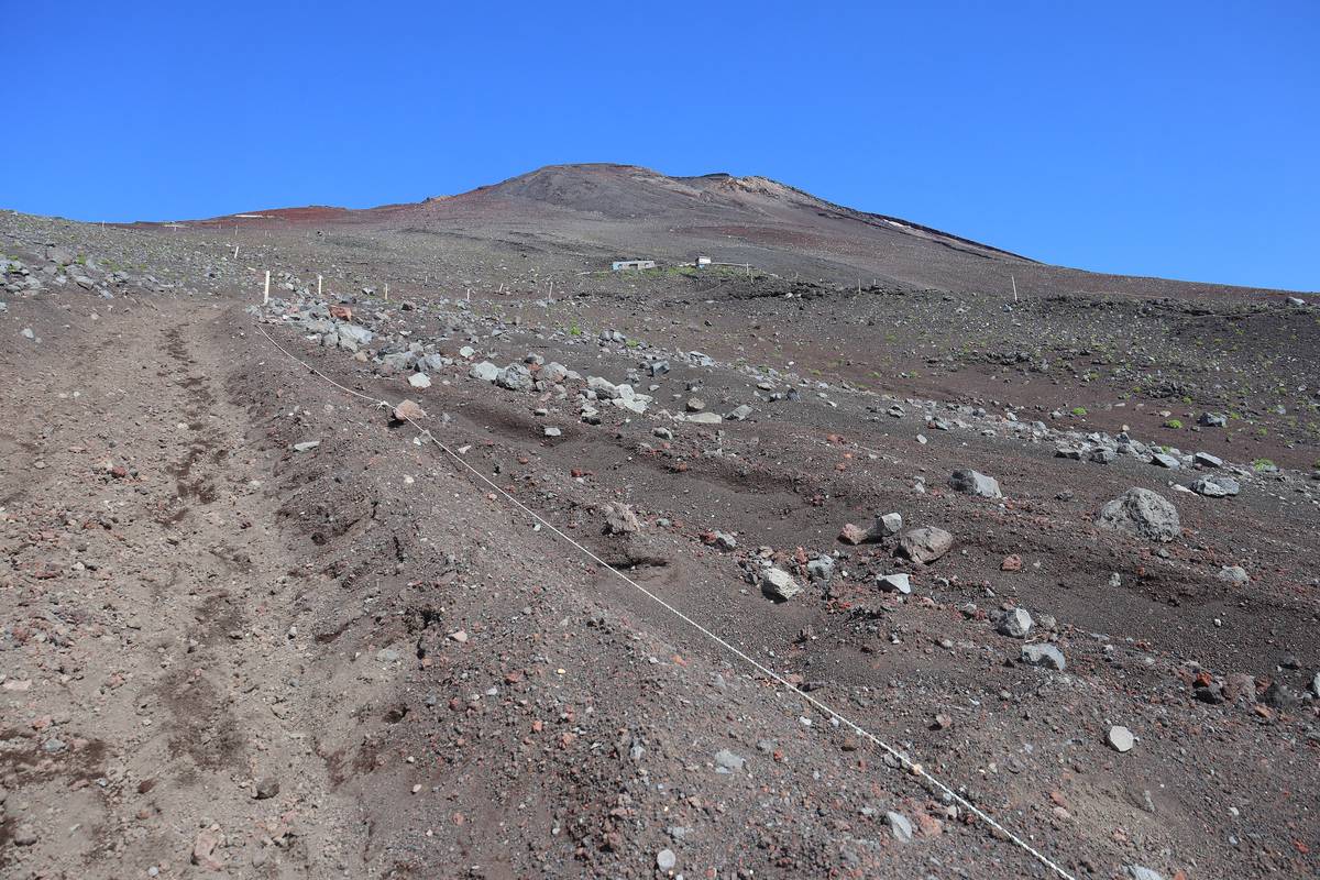The Osunabashiri descent on Mount Fuji: a strip of soft brown volcanic sand pocked with deep heel prints, separated by a white rope on stakes from a field of black scoria at right