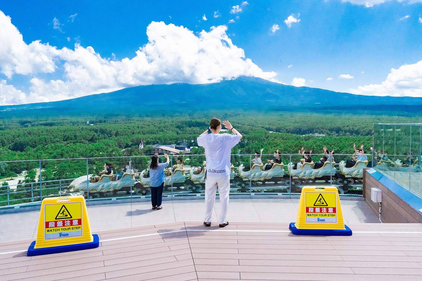 從 FUJIYAMA タワー展望甲板看 FUJIYAMA 過山車列車呼嘯而過，乘客舉手，背景樹海延伸到富士山山腳