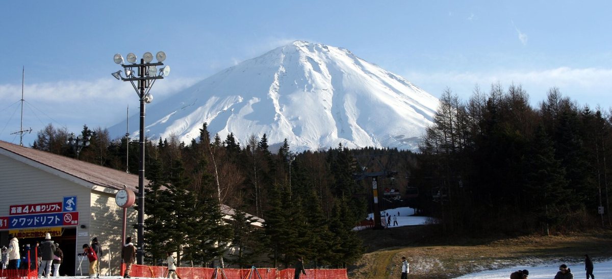ふじてん滑雪場山麓：左側是掛著「クワッドリフト」招牌的纜車站，樹林上方是整面積雪的富士山