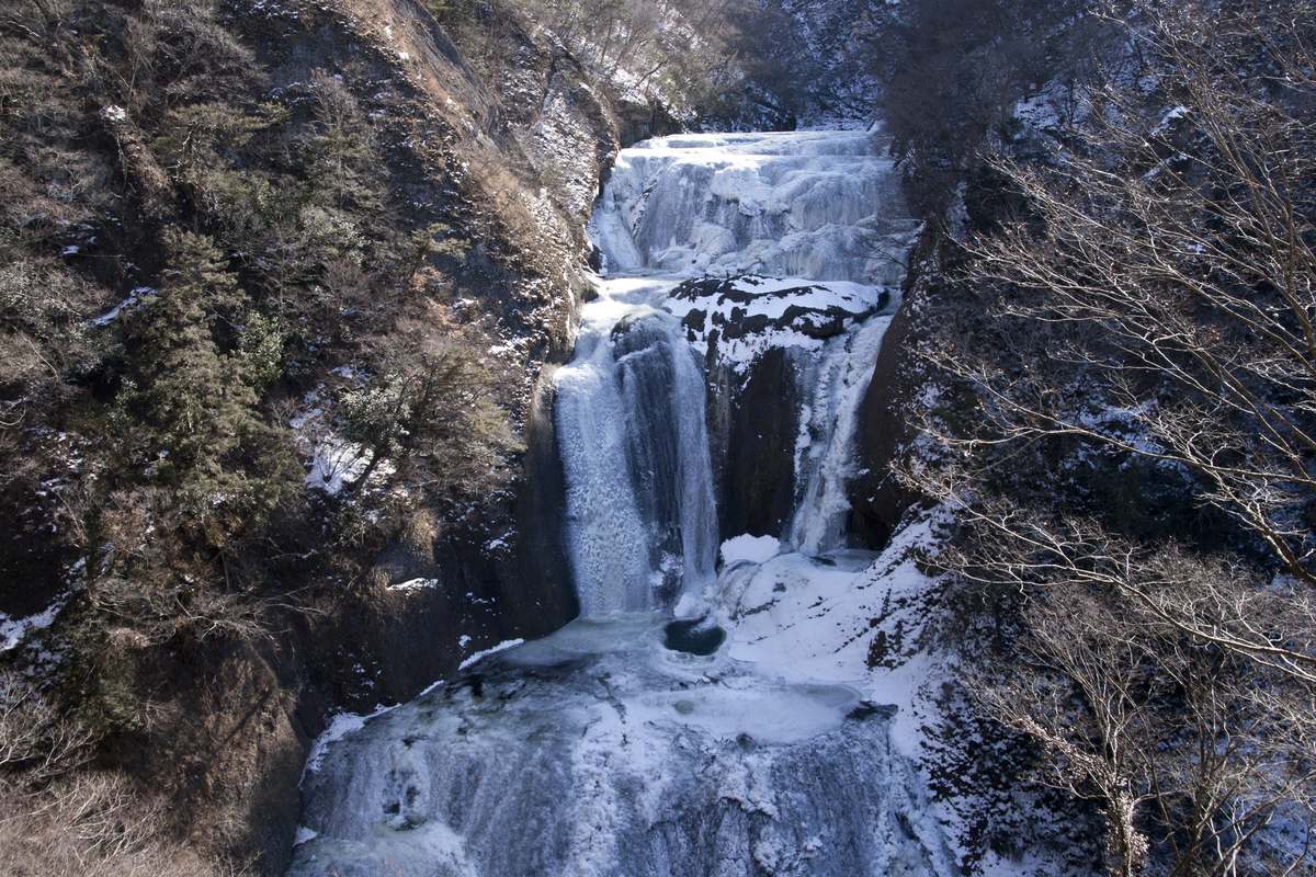 從高處俯看結冰的袋田瀑布全景:上段岩壁結成連片白冰,中段有一道水流仍在落下,下方河床與兩側山坡積雪