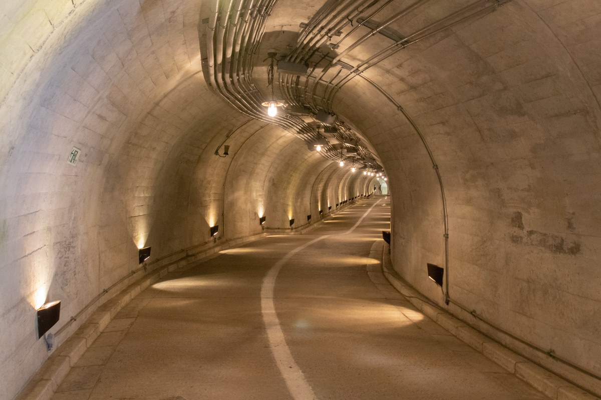 袋田瀑布觀瀑隧道內部:混凝土拱形隧道向右彎,地面有一條白色導引線,兩側牆腳的嵌燈把牆面打成暖黃色,看不到盡頭