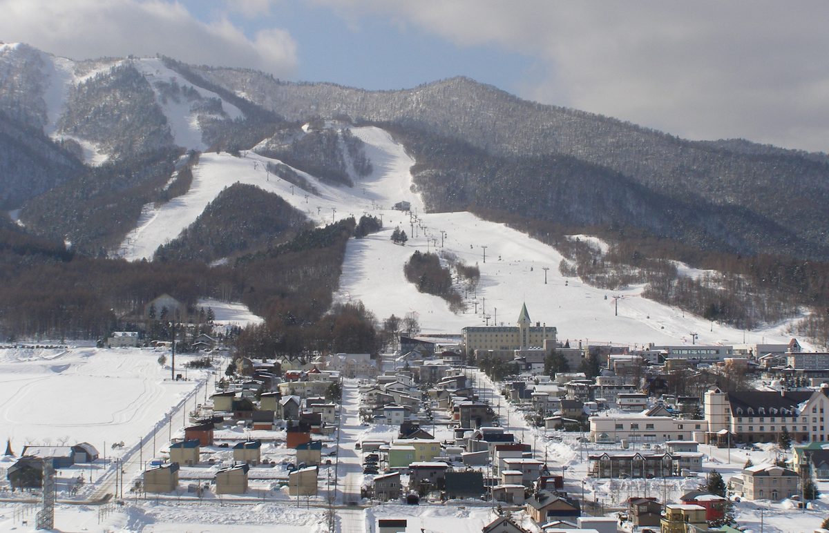 從高處看富良野滑雪場北之峰區:幾條寬雪道從山腰滑到山腳,雪道上有成排的吊椅支柱與空中吊籃車廂,山腳緊接著一整片積雪的旅館與民宅
