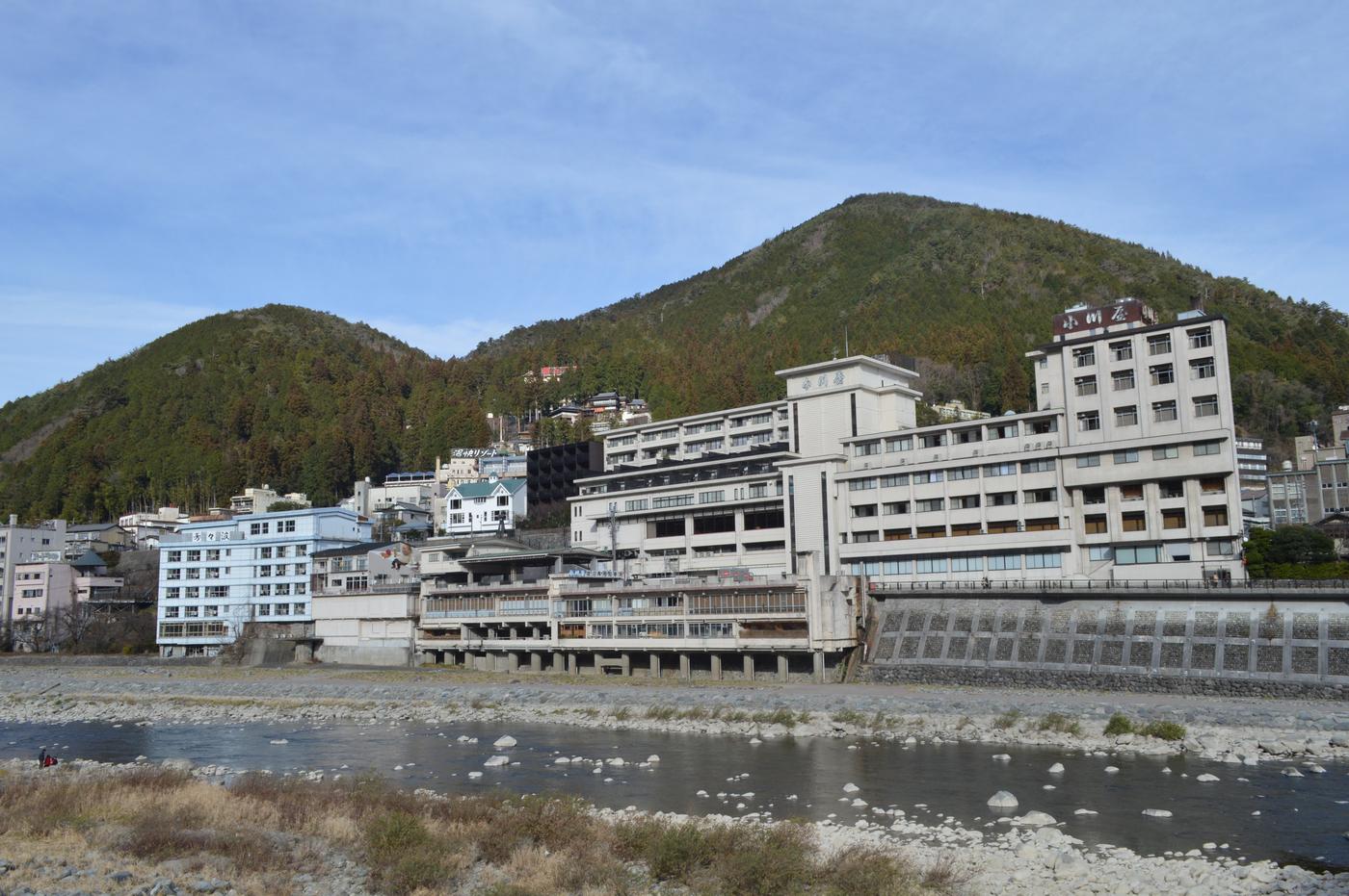 飛驒川河灘對岸,沿著河岸蓋起的多層溫泉旅館,最高那棟屋頂招牌寫著「小川屋」,背後是兩座長滿樹的山