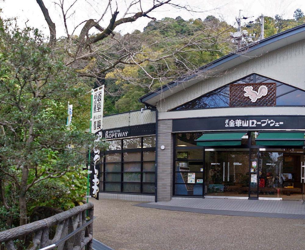 岐阜公園裡的金華山纜車山麓站：灰白色建築正面掛著黑底白字的「ぎふ金華山ロープウェー」招牌，三角形山牆上有松鼠圖案，左邊另一塊招牌寫 KINKAZAN ROPEWAY，入口是玻璃自動門，背後是金華山的樹林