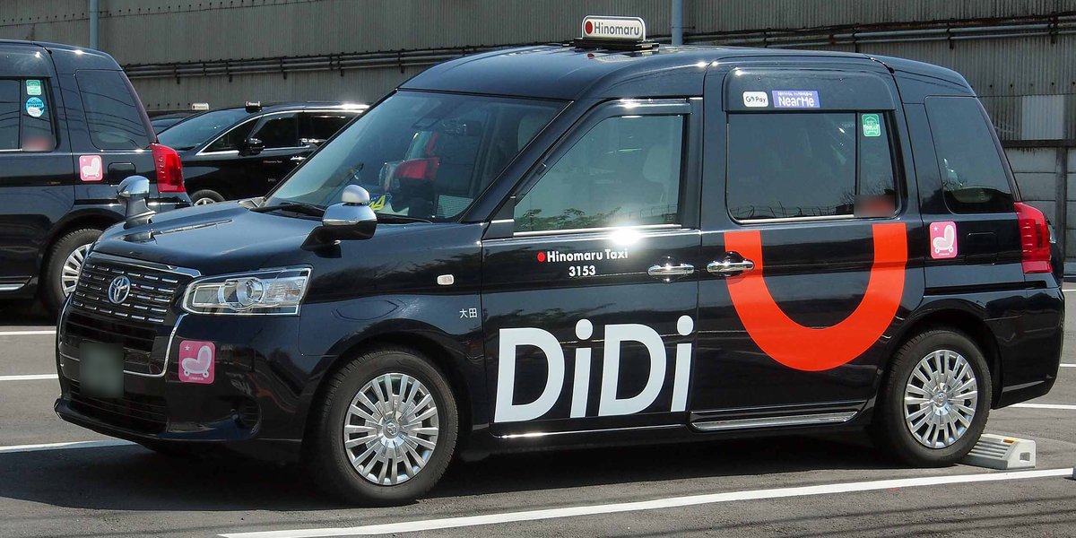停在停車格裡的黑色 JPN TAXI，車身印著大大的白色「DiDi」字樣與橘色弧線，車門上寫著 Hinomaru Taxi 3153