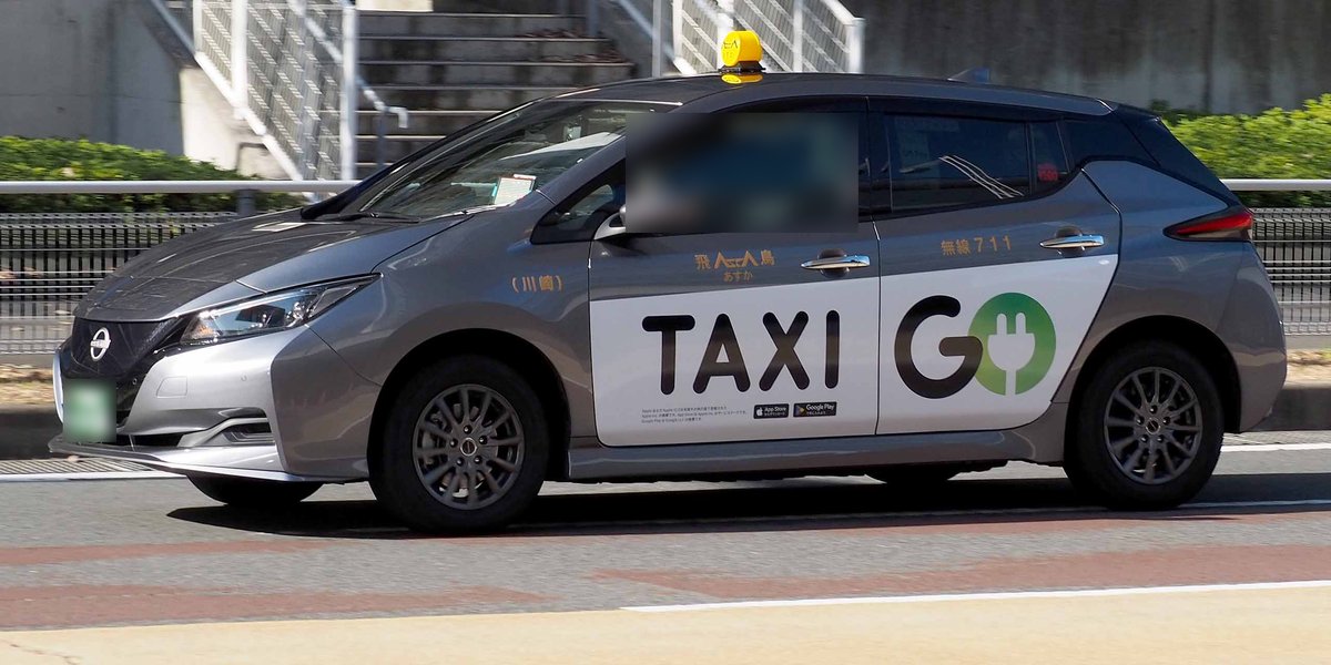 銀灰色日產 Leaf 計程車側面，車門貼著白底黑字的「TAXI GO」廣告與 App Store、Google Play 標誌，車頂是黃色車頂燈，車門上印著車行名「飛鳥」與無線編號 711