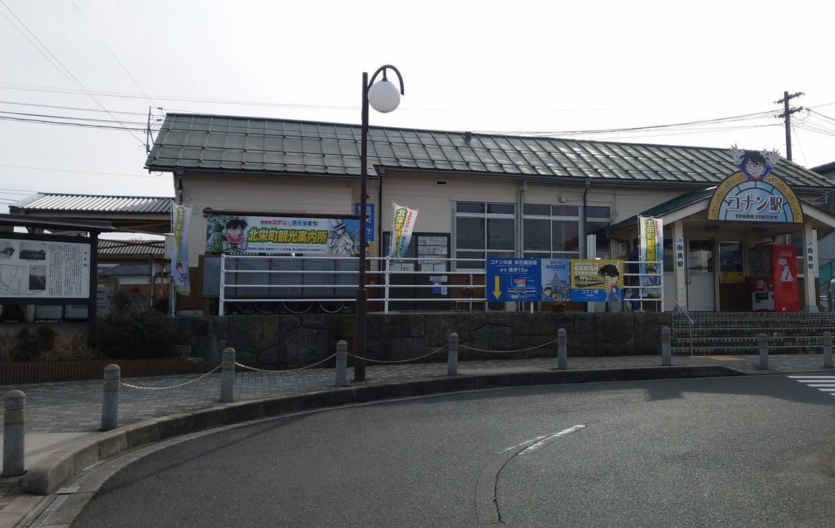 陰天的 JR 由良站站房,右邊入口上方是柯南造型的「コナン駅」招牌,左半邊外牆掛著「北栄町観光案内所」橫幅,欄杆上並排著往米花商店街徒步 10 分的導覽牌