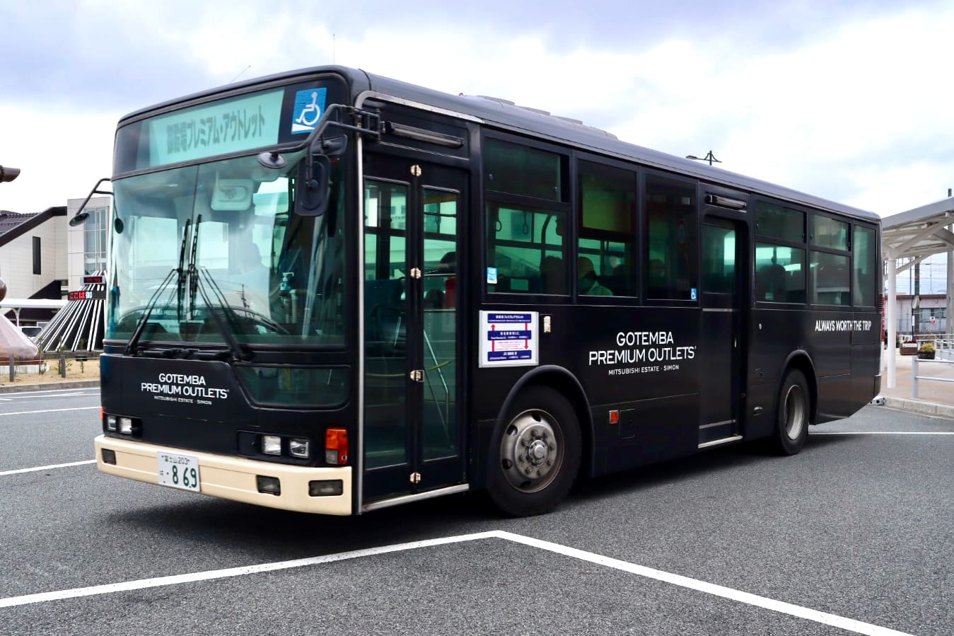 An all-black shuttle bus parked in a station forecourt, GOTEMBA PREMIUM OUTLETS and MITSUBISHI ESTATE·SIMON lettered in white on the side, the front blind reading Gotemba Premium Outlets in Japanese