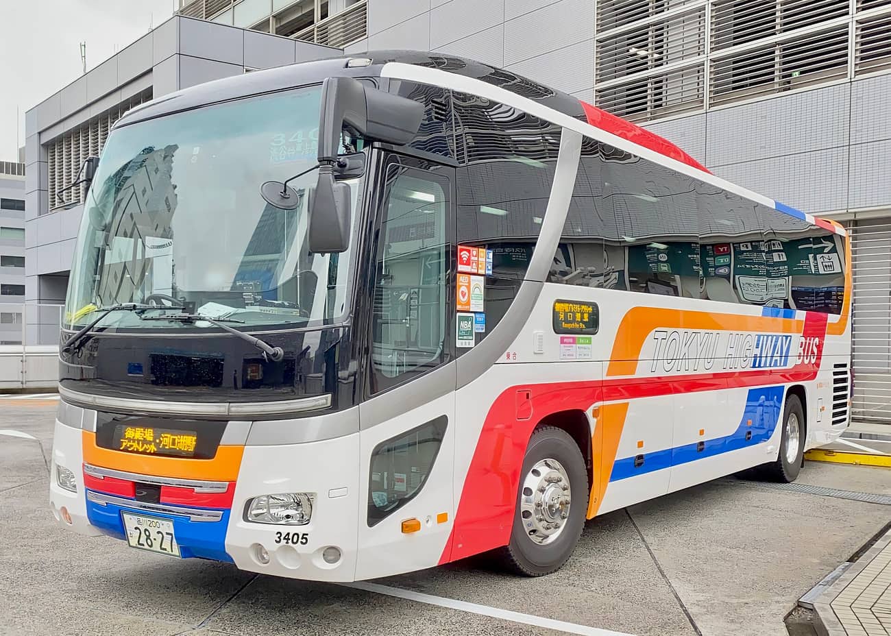 A white highway coach with red, orange and blue striping, its front destination blind reading Gotemba Outlet / Kawaguchiko Station in Japanese, TOKYU HIGHWAY BUS lettered along the side