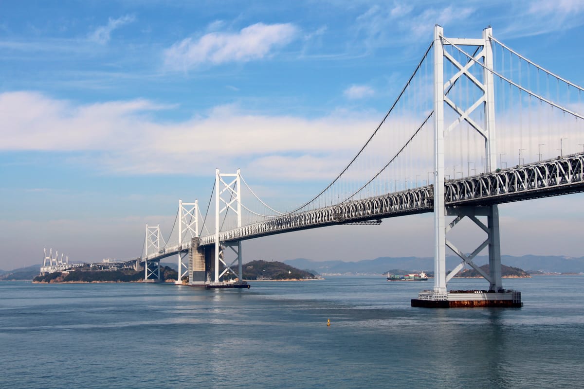 Wide view of the Minami Bisan-Seto section of the Great Seto Bridge, its white suspension towers striding across the Seto Inland Sea on piers built in open water