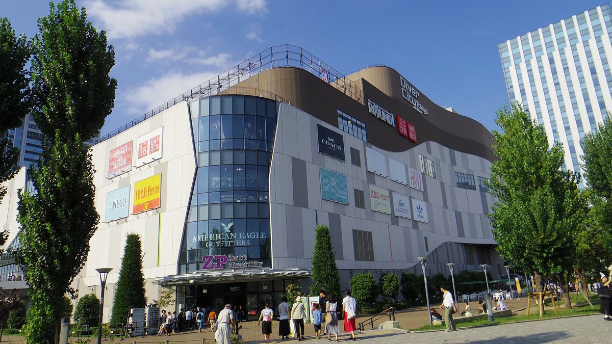 DiverCity 東京 Plaza 的外觀:白灰色外牆上掛著 UNIQLO、COACH、H&M 等品牌招牌,咖啡色弧形頂樓寫著「DiverCity Tokyo Plaza」,一樓是 Zepp DiverCity 的入口,行人走在兩旁種著行道樹的廣場上