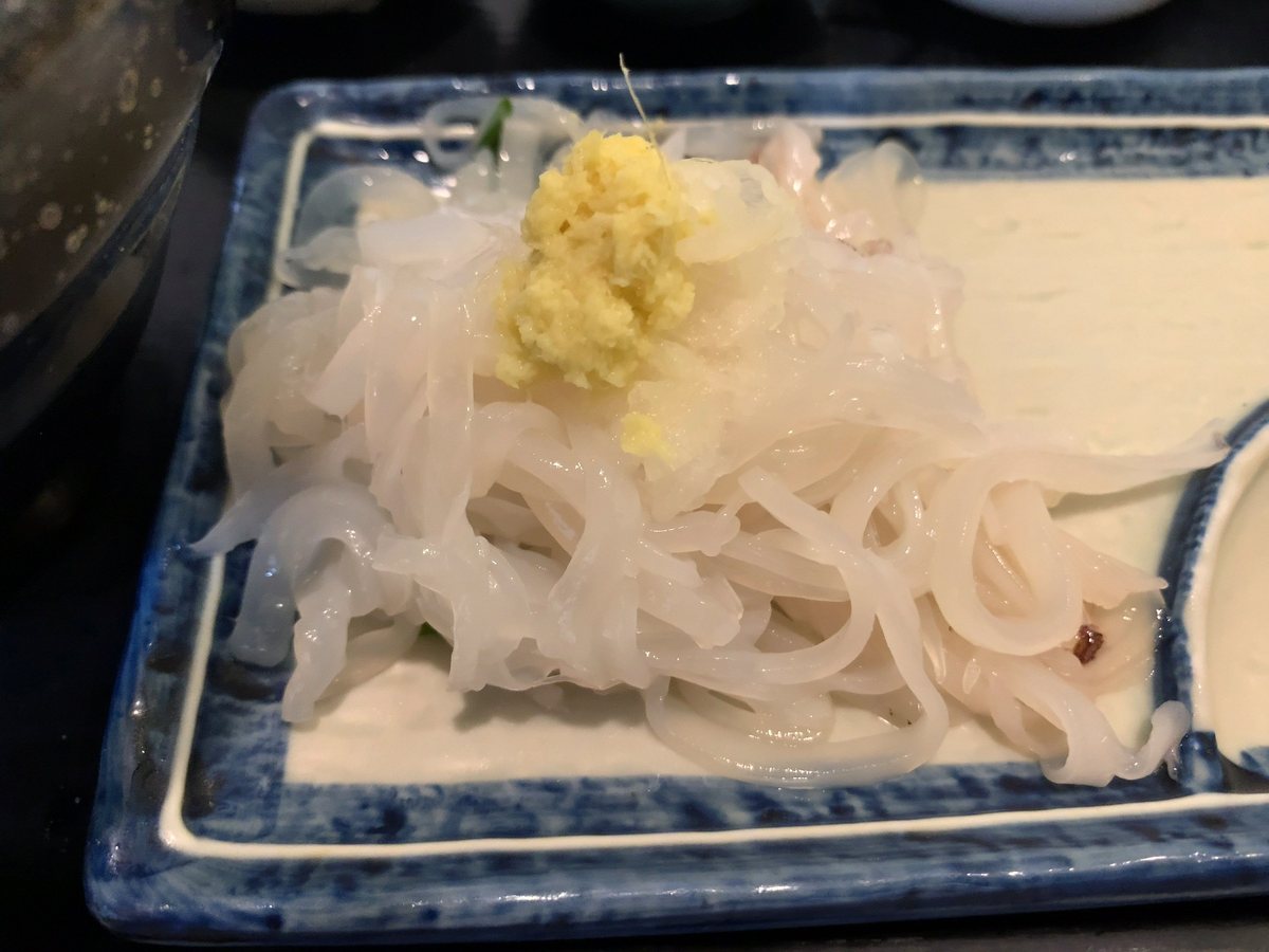藍白花紋的長方盤上，一堆切成細麵條狀、半透明帶白色的烏賊生魚片，上面放著一小坨黃色的薑泥