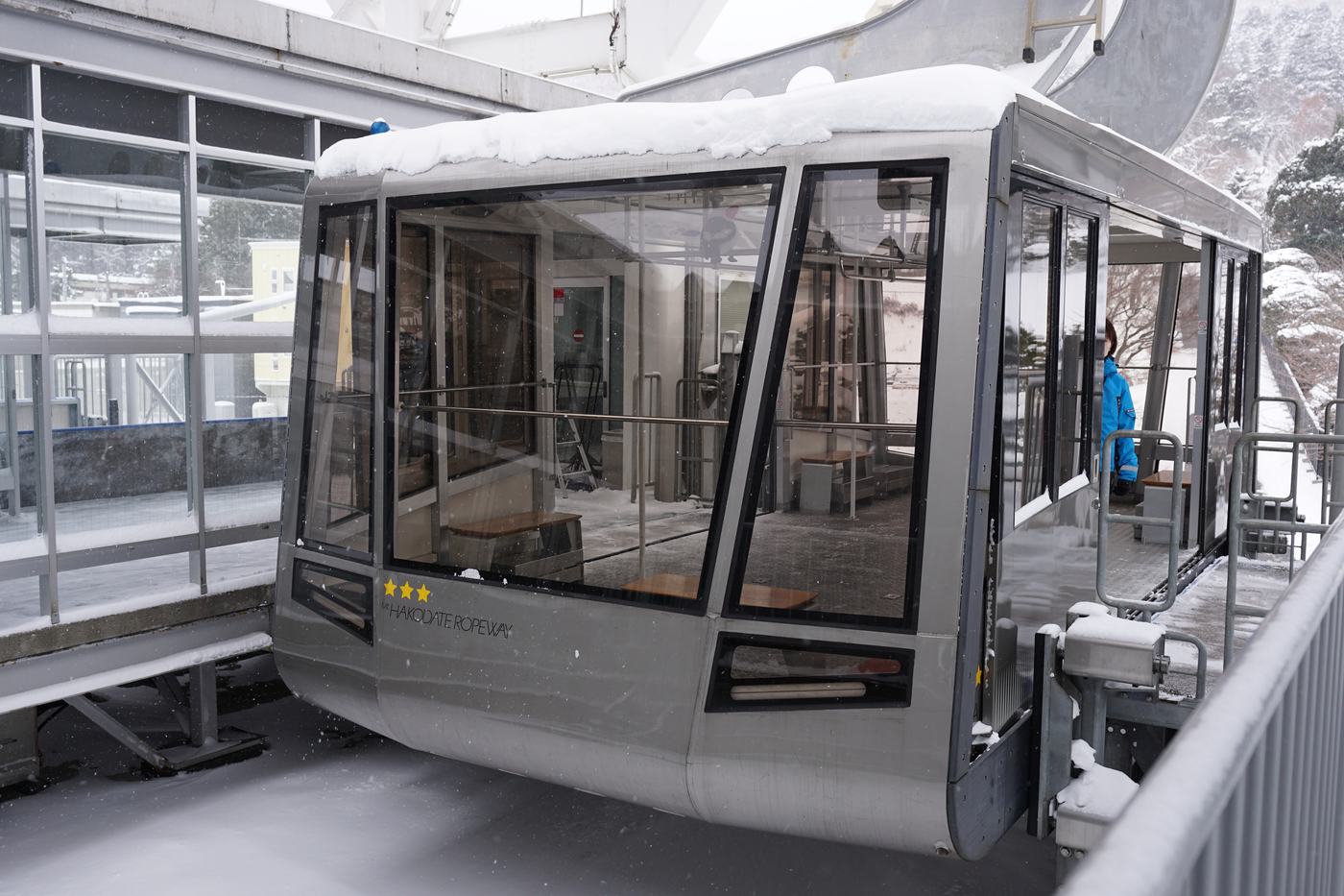 函館山纜車現行車廂停靠在車站月台,車頂積著雪,車身印著 MT.HAKODATE ROPEWAY 與三顆星