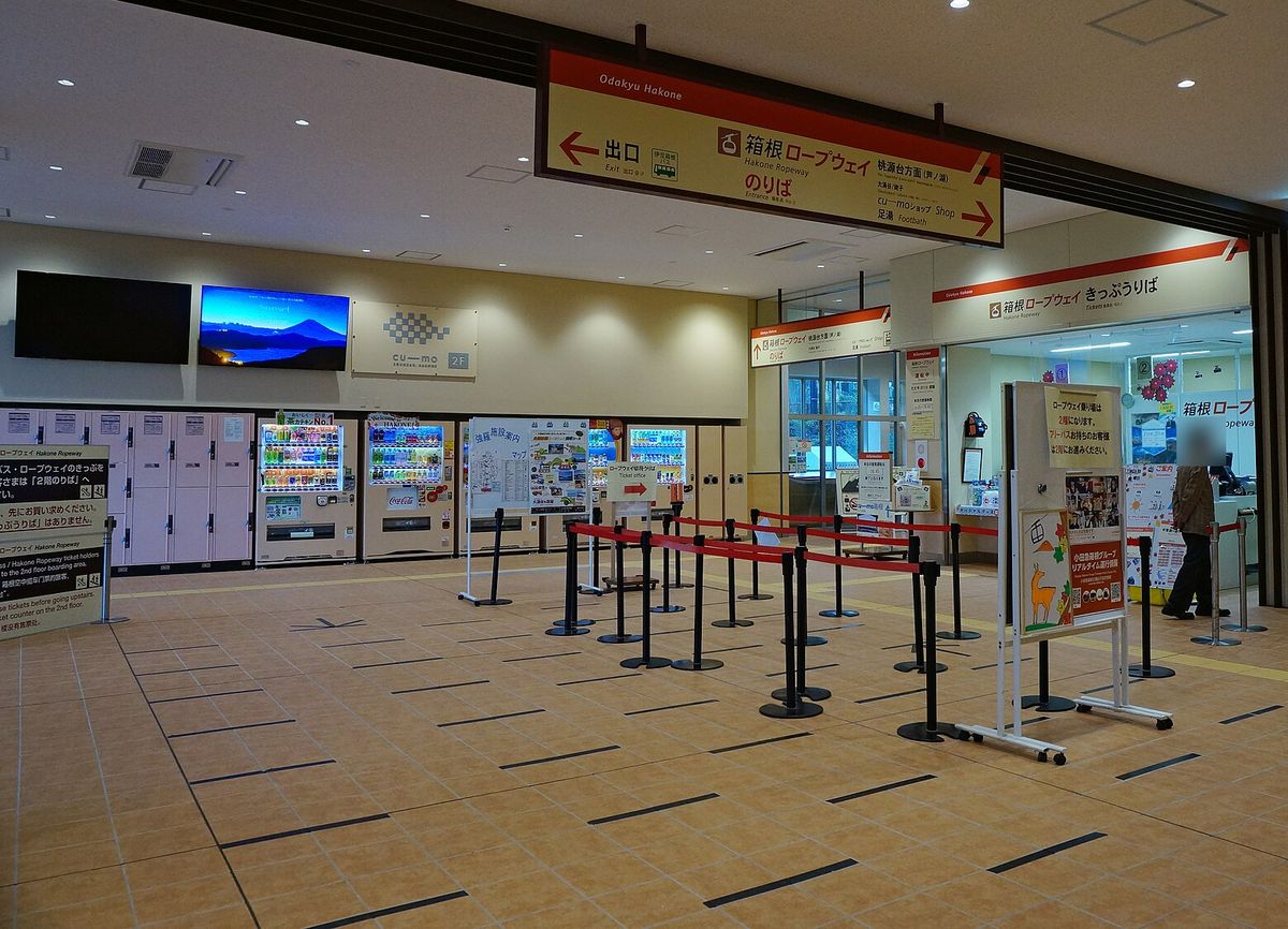 早雲山站一樓大廳:天花板吊著橘黃色指標「箱根ロープウェイ のりば」與「出口」,右側是「箱根ロープウェイ きっぷうりば」售票窗口,前面拉著紅色排隊線,左側是置物櫃與自動販賣機(2021 年 11 月拍攝)