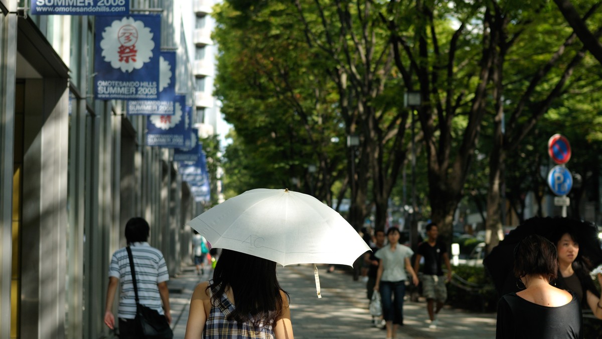 A Japanese street in midsummer under strong sun, pedestrians walking under parasols