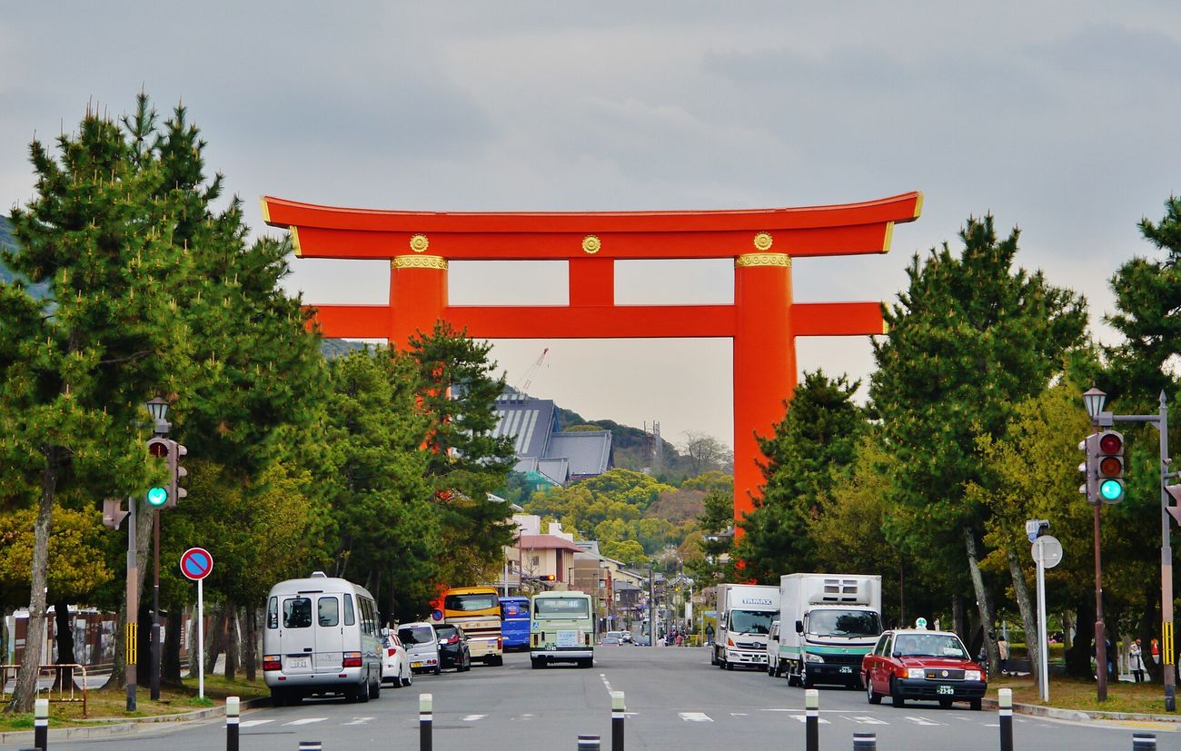 The vermillion great torii of Heian Jingu straddling Jingu-michi avenue, framed by pines and city traffic