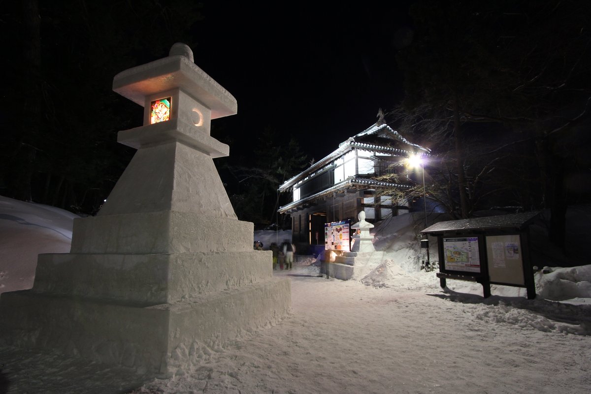 夜裡一座比人還高的雪燈籠,做成石燈籠的形狀、底座是三層方形雪台,火袋的窗口嵌著一片彩繪畫片從裡面透光,後方是打燈的兩層城門與園內案內圖看板