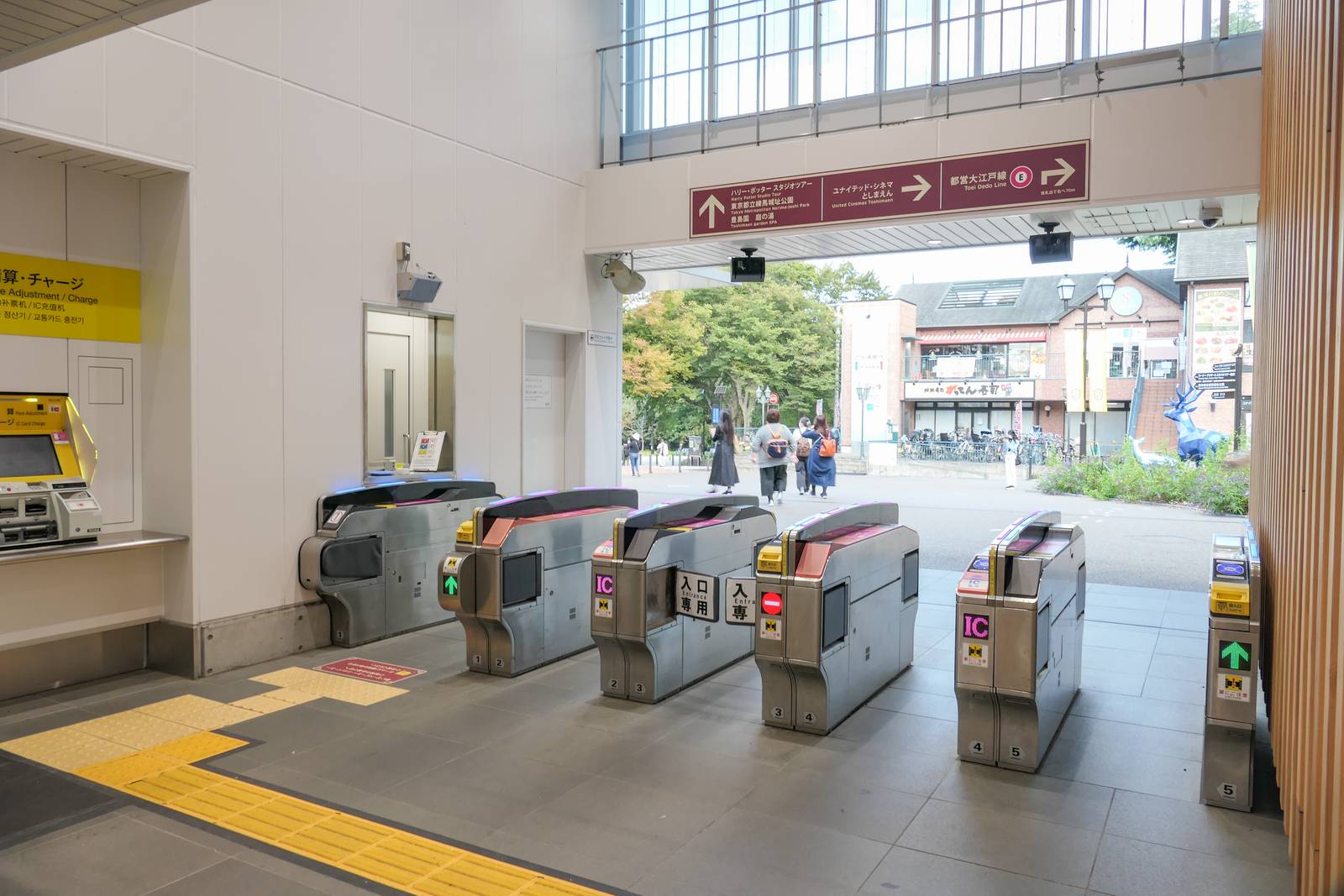 西武豊島園站剪票口，上方紅褐色指示牌：向上箭頭指「ハリー・ポッター スタジオツアー」「東京都立練馬城址公園」「豊島園 庭の湯」，向右箭頭指「ユナイテッド・シネマ としまえん」，另一個右轉箭頭指「都営大江戸線 改札出て右へ70m」；剪票口外是綠樹與站前街道