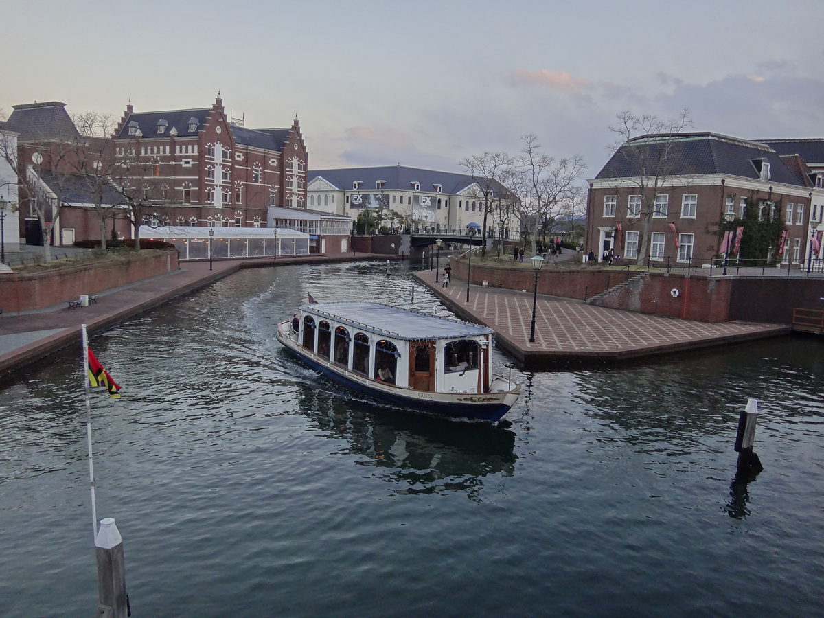 A canal cruiser carrying passengers along the canal at Huis Ten Bosch, flanked by red-brick Dutch buildings and brick quays