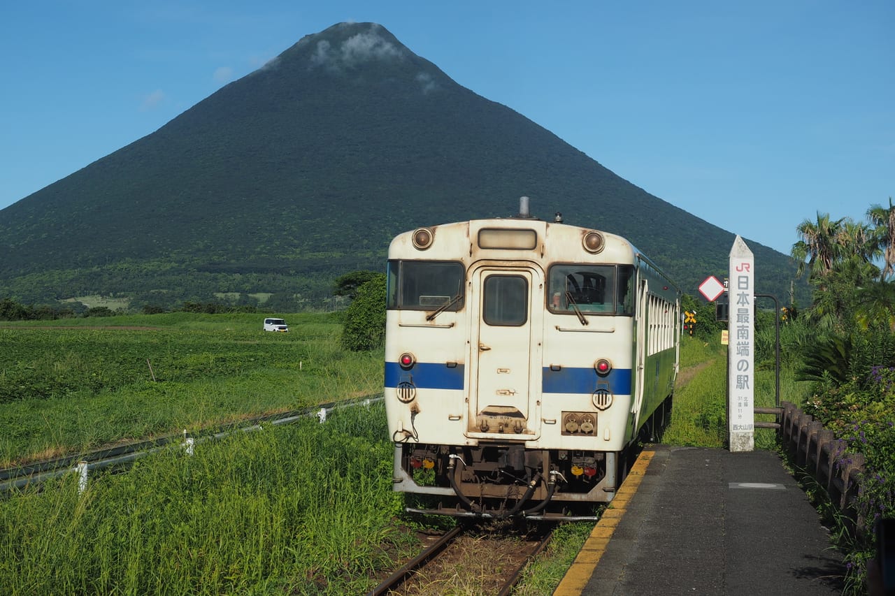 A local train passing near JR Nishi-Oyama Station with the symmetrical cone of Mt. Kaimon behind