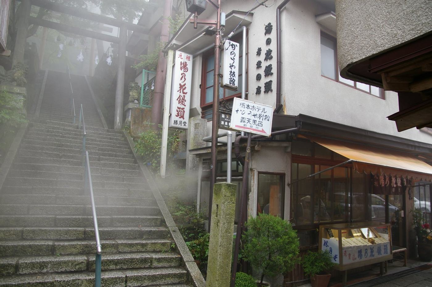 霧氣中的伊香保石段街末段，石階盡頭立著伊香保神社的木造鳥居，右側是掛著湯乃花饅頭招牌的店家