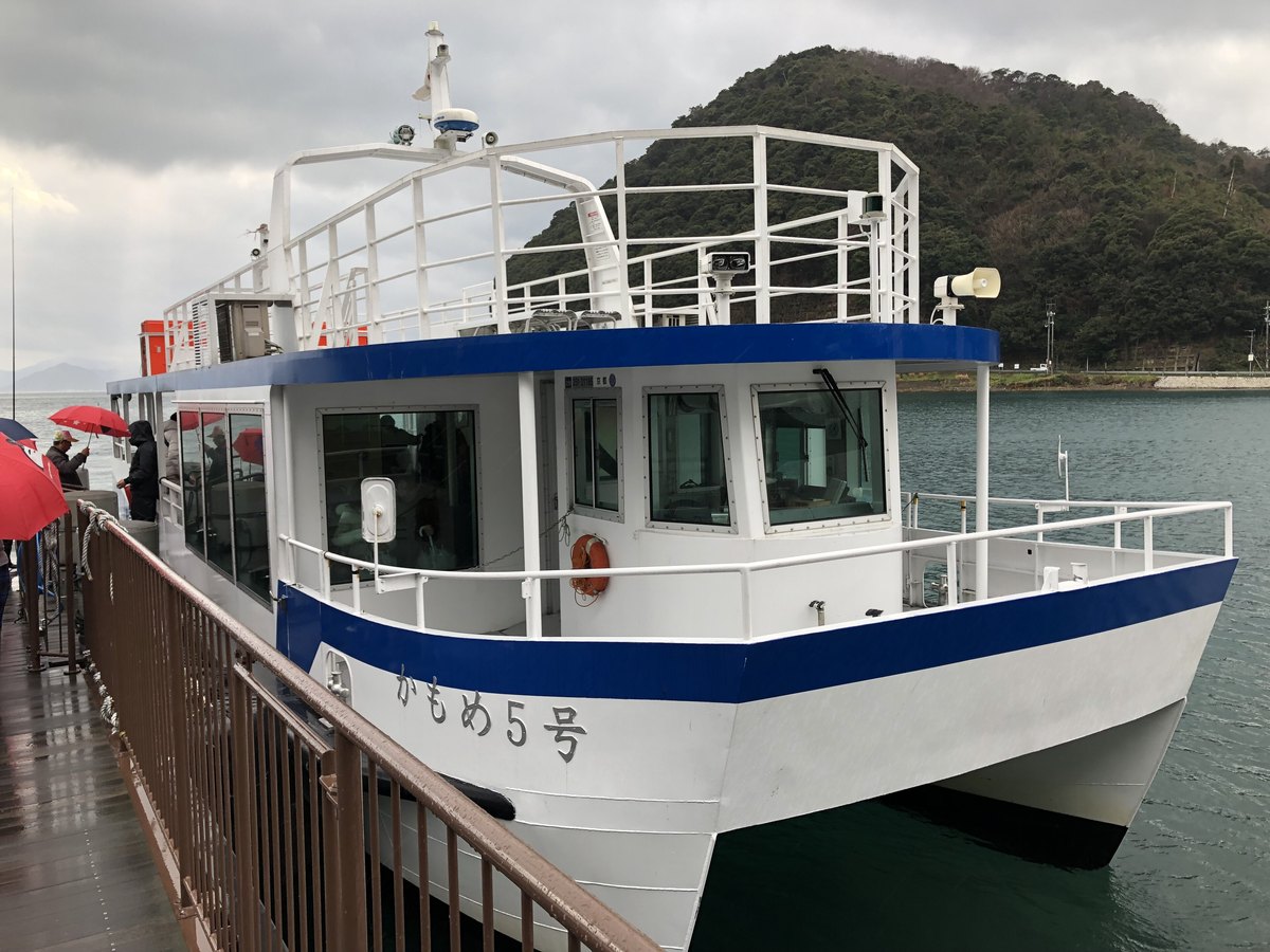 The Ine Bay sightseeing boat Kamome No. 5 moored alongside a pier on a rainy day, passengers waiting under umbrellas