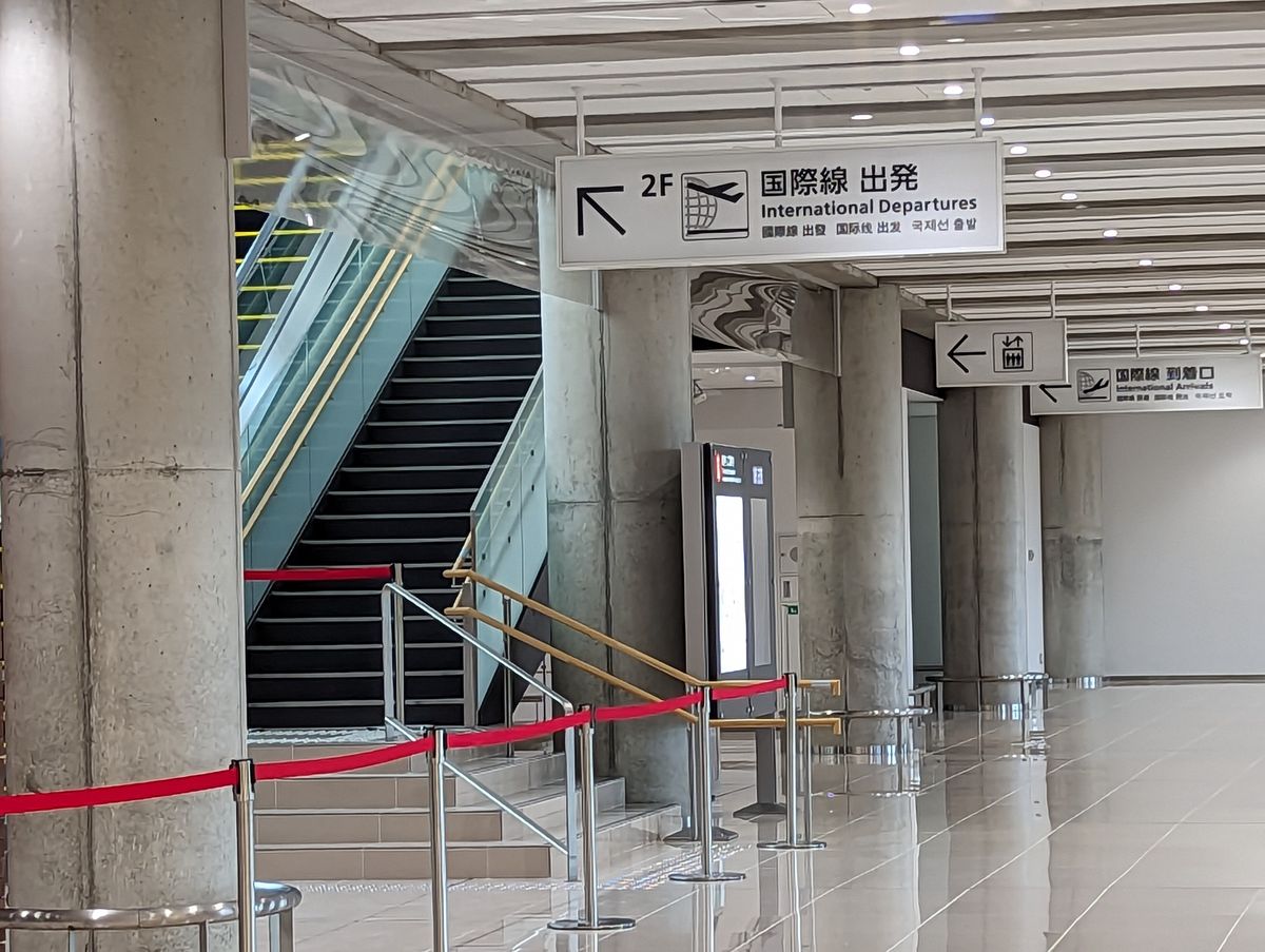 南ぬ島石垣空港航廈一樓,天花板吊著「2F 國際線出發」指標(日、英、繁中、簡中、韓文),左邊是往二樓的樓梯與手扶梯,右後方另一塊指標寫著國際線到着口