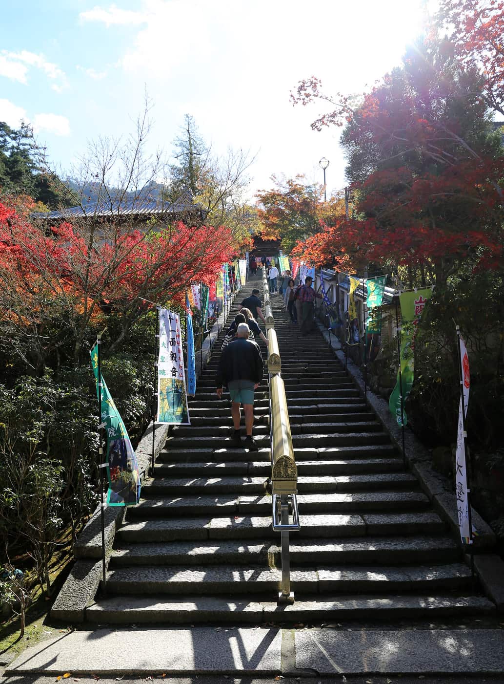 The stone stairway of Daisho-in temple on Miyajima lined with banners naming the eleven-headed Kannon, with autumn foliage overhead