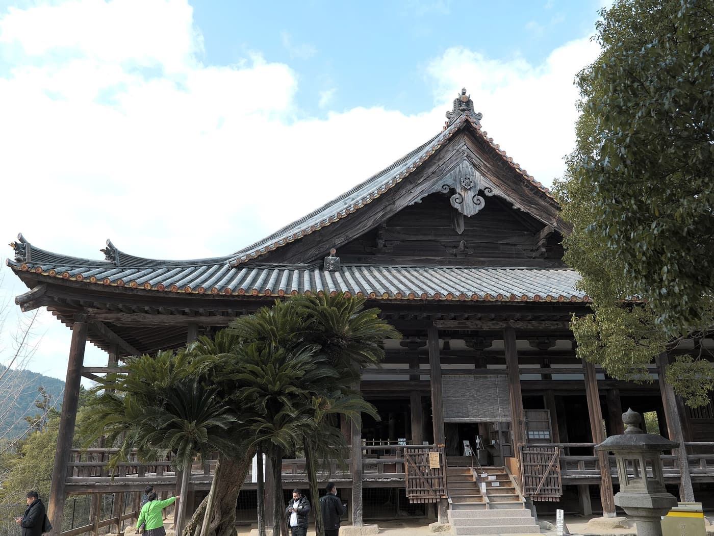 The vast open timber hall of Senjokaku (Toyokuni Shrine) on Miyajima, with visitors walking beneath its eaves