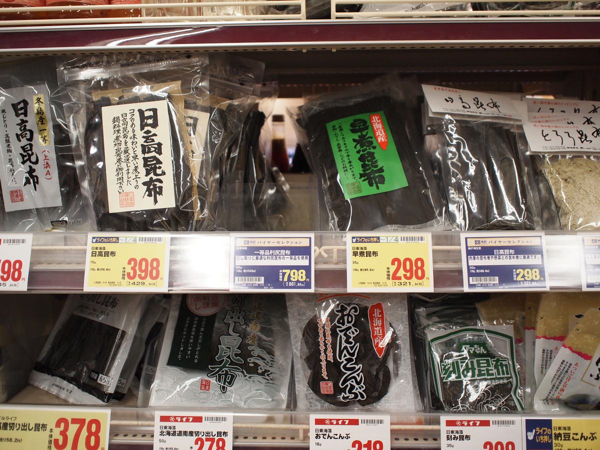 Dried kombu in clear packets on a Japanese supermarket shelf, labelled Hidaka kombu and Hokkaido-grown with gram weights and yen prices