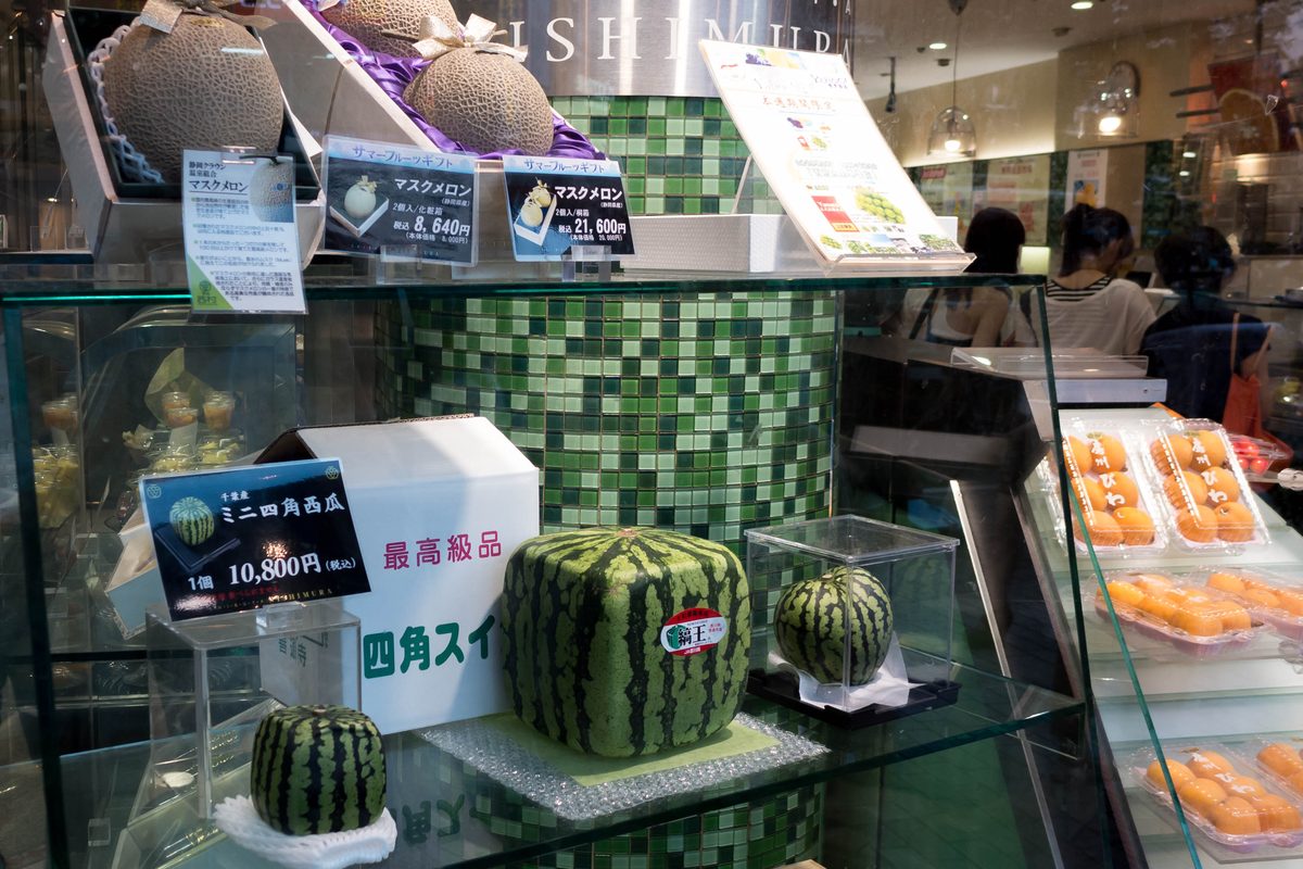 Window of a high-end fruit shop in Shibuya, Tokyo, showing ribbon-tied netted muskmelons in presentation boxes and square watermelons with yen price cards