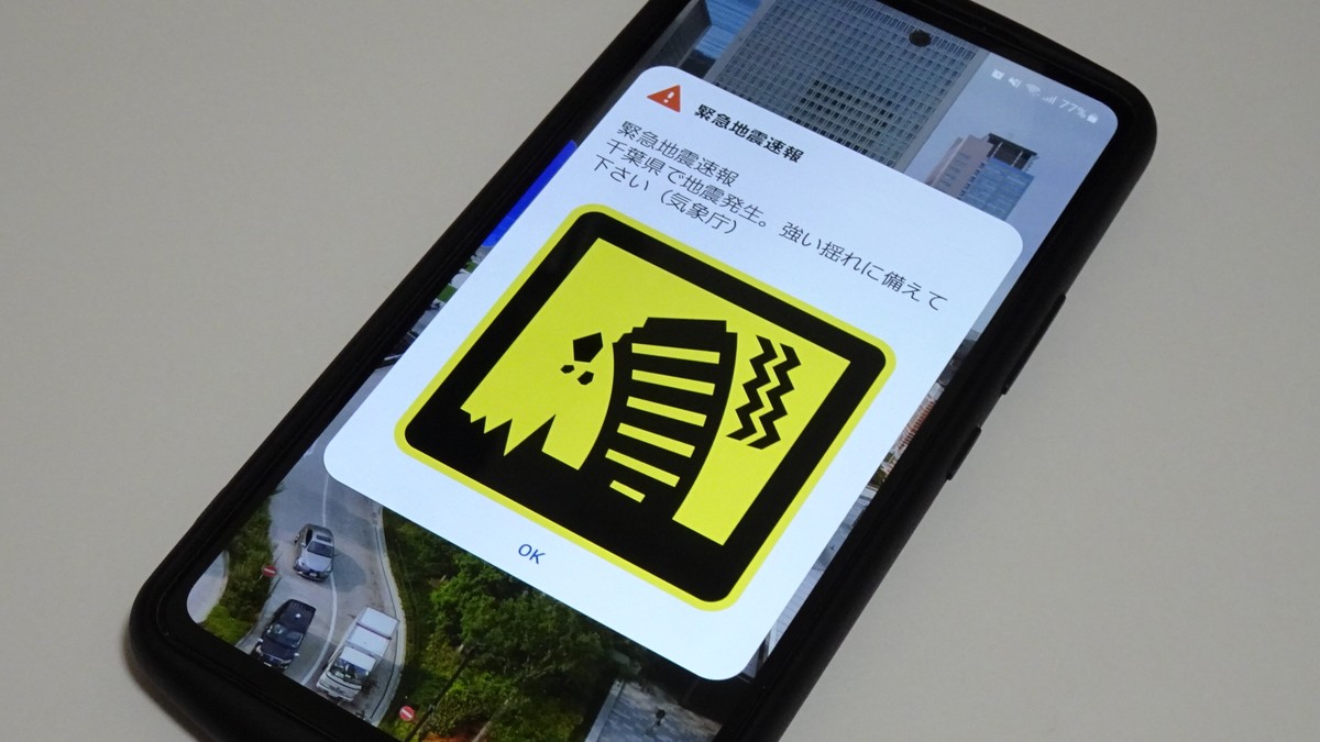 A Japanese phone screen displaying an Earthquake Early Warning alert on a yellow background, with the affected region listed below the headline