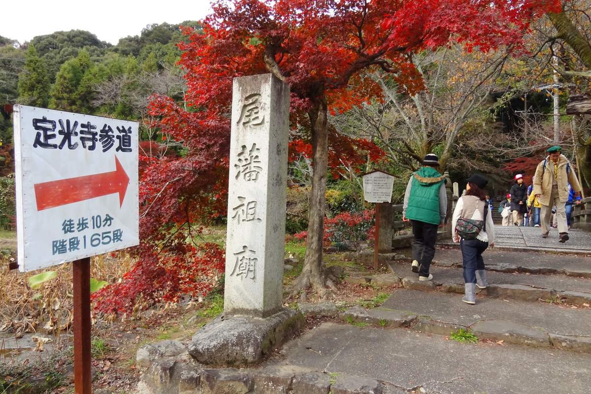 The signpost at the entrance to Jokoji's approach path beside the Owari domain founder's mausoleum stone marker, with red maples and stone steps behind