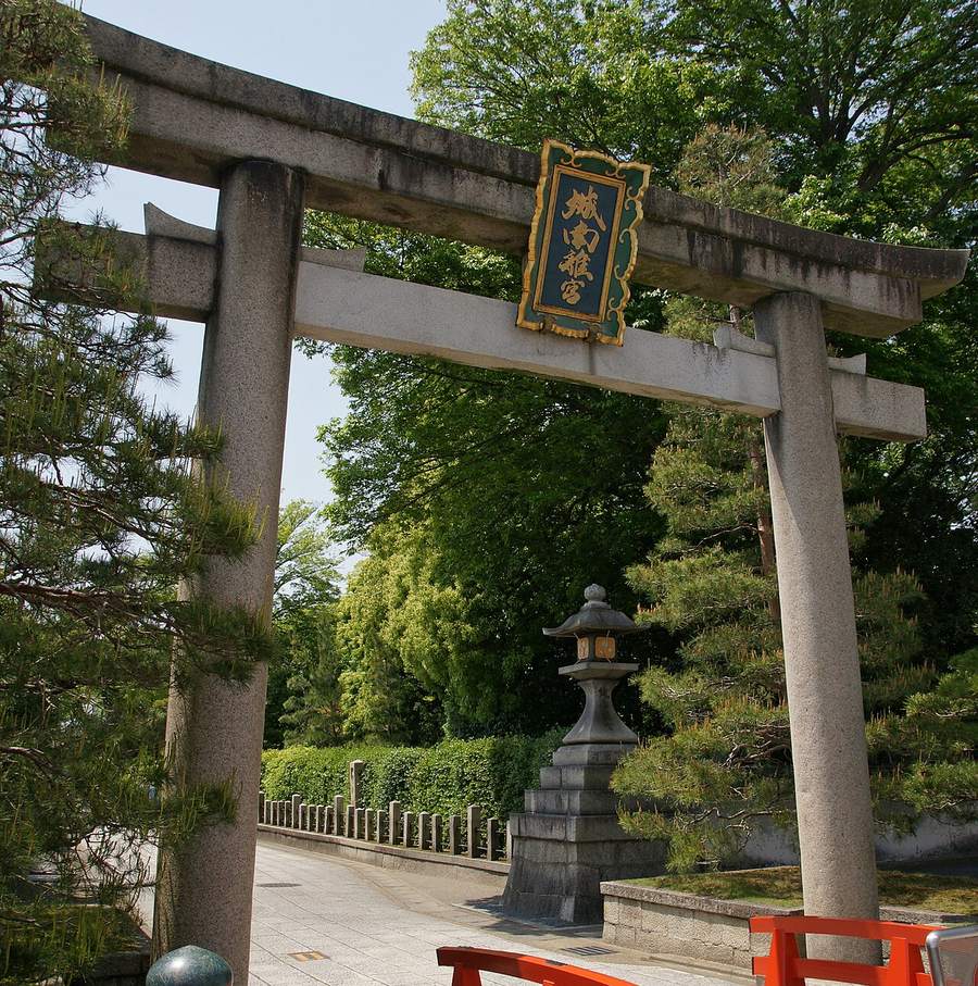 城南宮東側的石造鳥居:橫樑中央掛著綠底金字的「城南離宮」匾額,鳥居後方是石燈籠與修剪整齊的樹籬,石板路往裡延伸