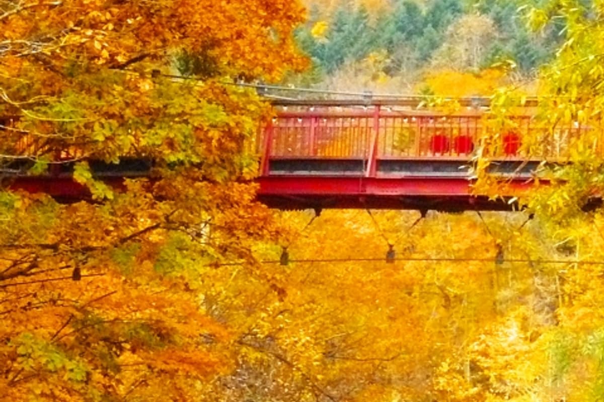 Jozankei Futami Suspension Bridge in autumn: red footbridge spans the Toyohira River gorge with foliage on both banks